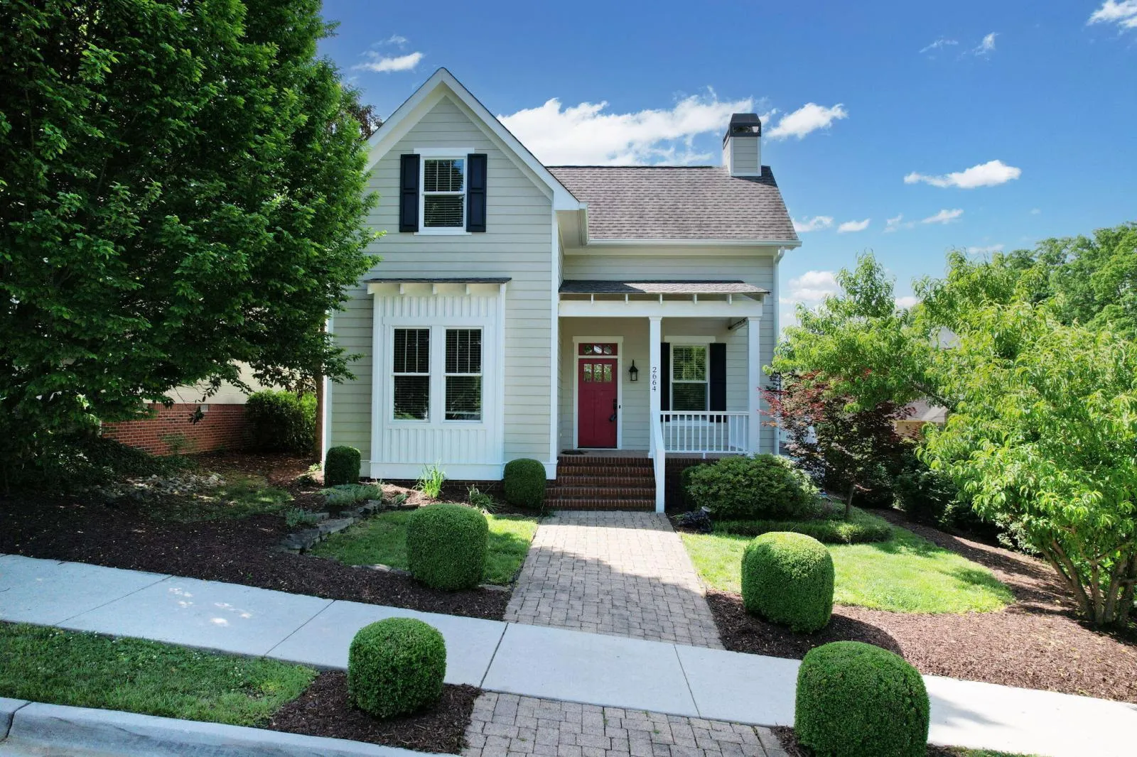 A white cottage-style home with a covered porch and red front door on a landscaped Cleveland, TN street